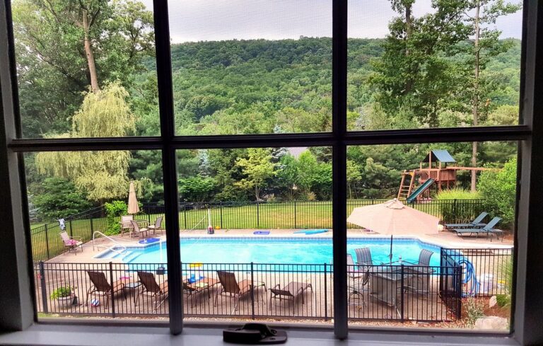 Sunny backyard with bright blue heated swimming pool surrounded by loungers
